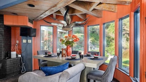 Un espace repas doté d’un plafond en bois, de grandes fenêtres et d’une table dressée pour quatre personnes.