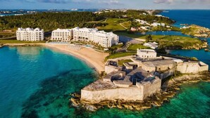 Luftaufnahme eines Küstenresorts mit breitem Strand, einer Festungsanlage und modernen Hotelgebäuden.