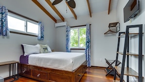 A bedroom with a wooden bed, two windows with curtains, a ceiling fan, and a TV mounted on the wall.