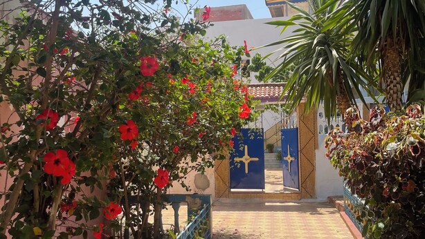Un chemin menant à un bâtiment doté d’une porte bleue ornée d’un symbole en forme de croix.