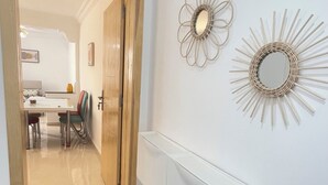 Un couloir avec une porte en bois, une console blanche et deux miroirs muraux ornés de motifs en forme de rayons de soleil.