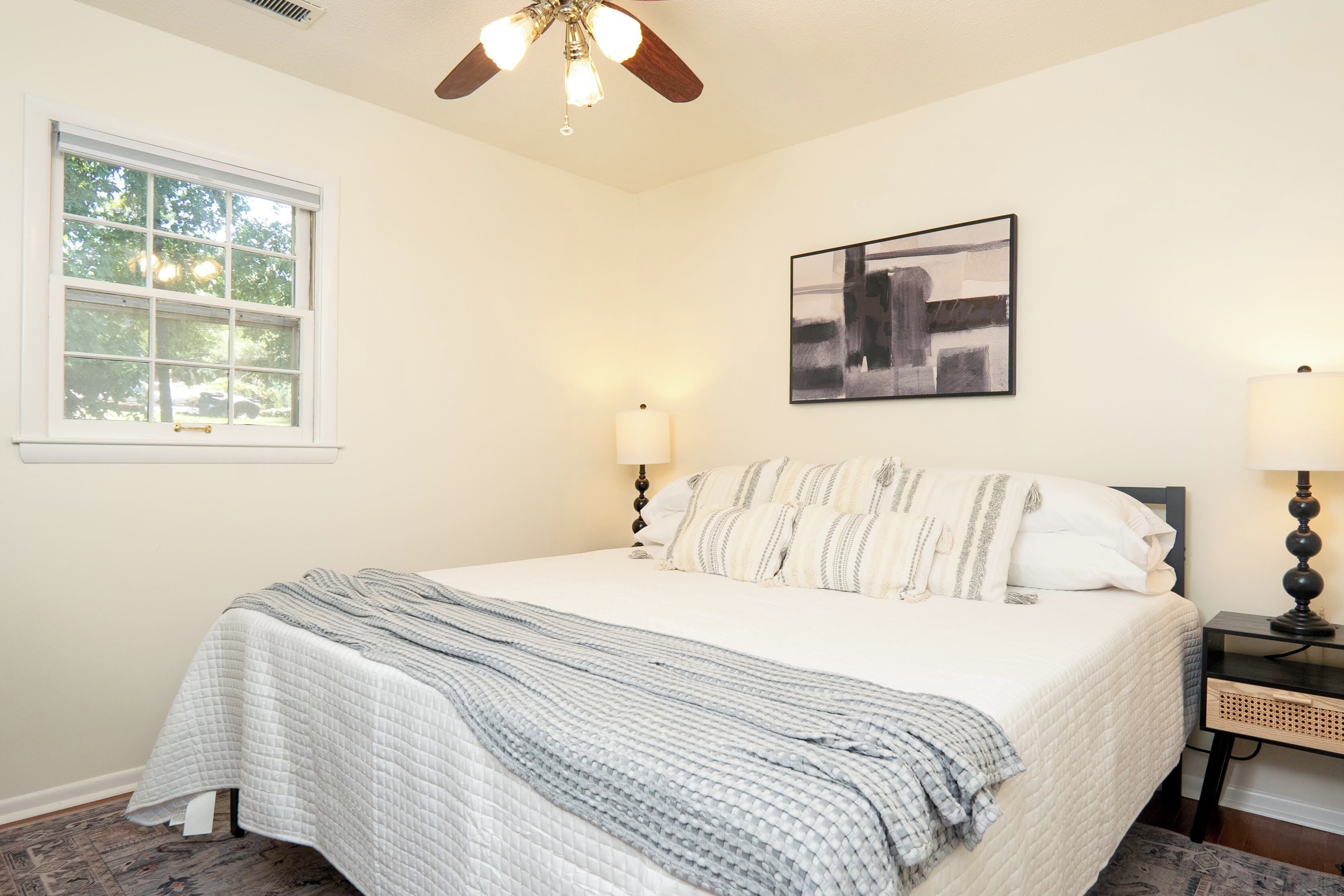 A neatly made bed with a quilted blanket, a bedside lamp, and a wall-mounted abstract painting.