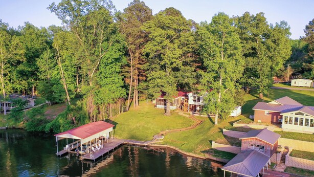 Une propriété au bord du lac, dotée d’un quai, d’une terrasse couverte et de plusieurs bâtiments entourés d’une forêt dense.