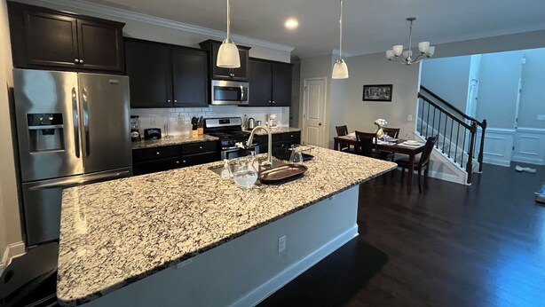 A modern kitchen with granite countertops, stainless steel appliances, pendant lighting, and a dining area with a staircase leading to another level. - Spacious 4-bedroom townhome with WiFi, AC in terrific Fort Mill (Fort Mill)