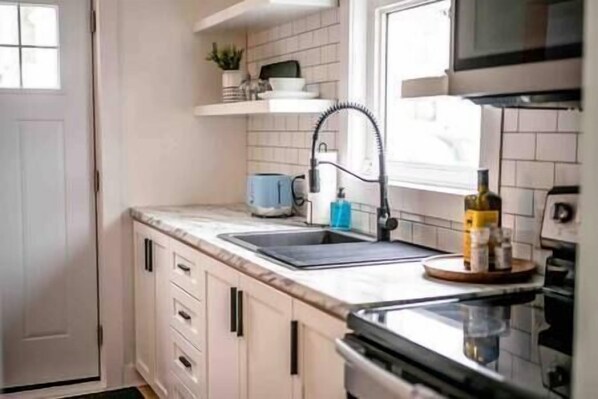 Cocina con alacenas blancas, un lavamanos, un microondas y una estufa.