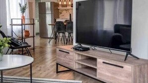 Een moderne woonkamer met een flatscreen televisie, een houten tv-meubel en een eethoek met stoelen en een tafel.