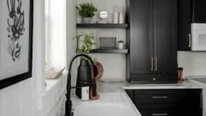 Une cuisine moderne avec des meubles noirs, un plan de travail blanc et un luminaire suspendu noir.