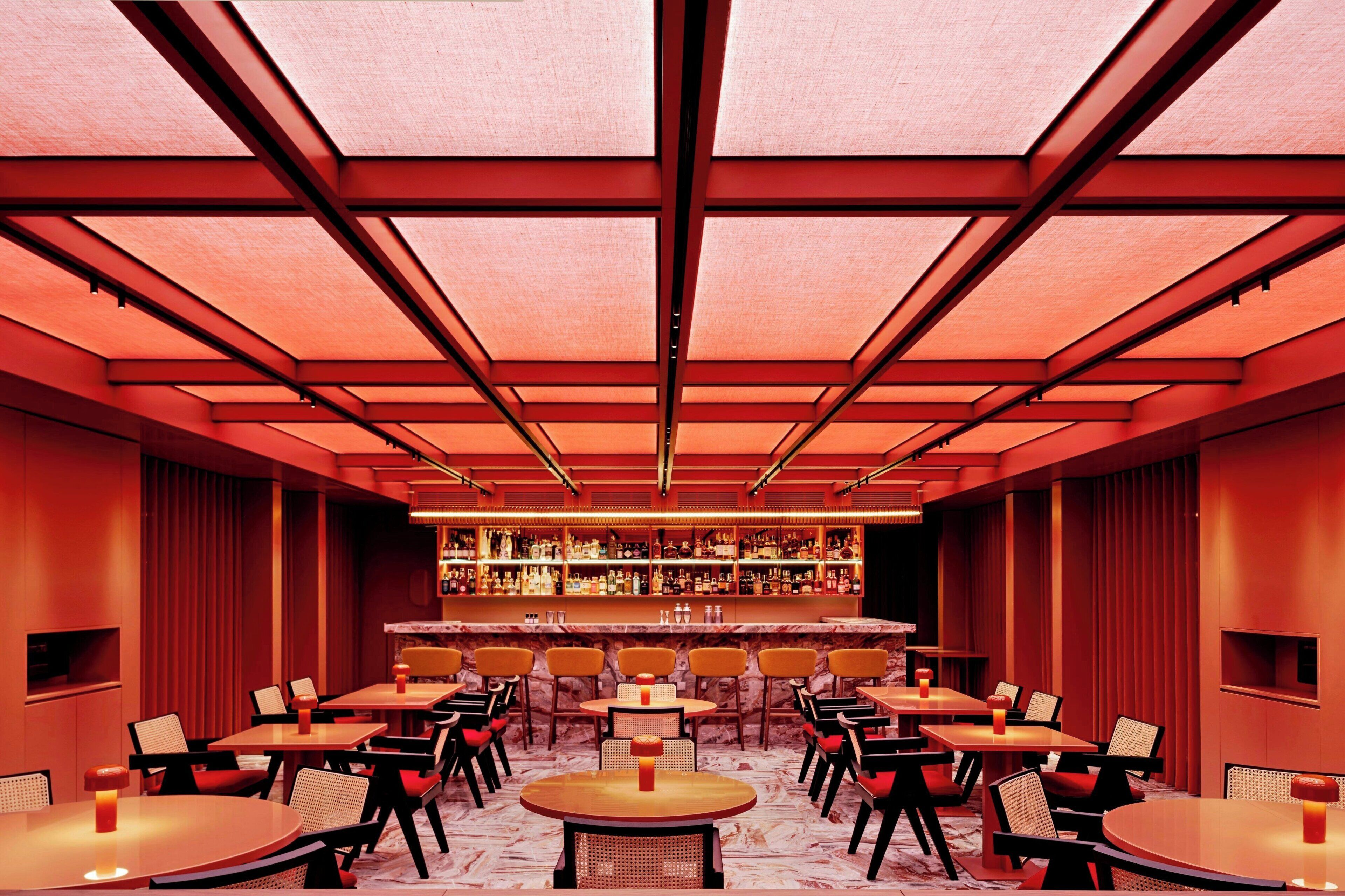 A bar area with multiple tables and chairs, a bar counter with bottles, and a ceiling with a grid pattern.