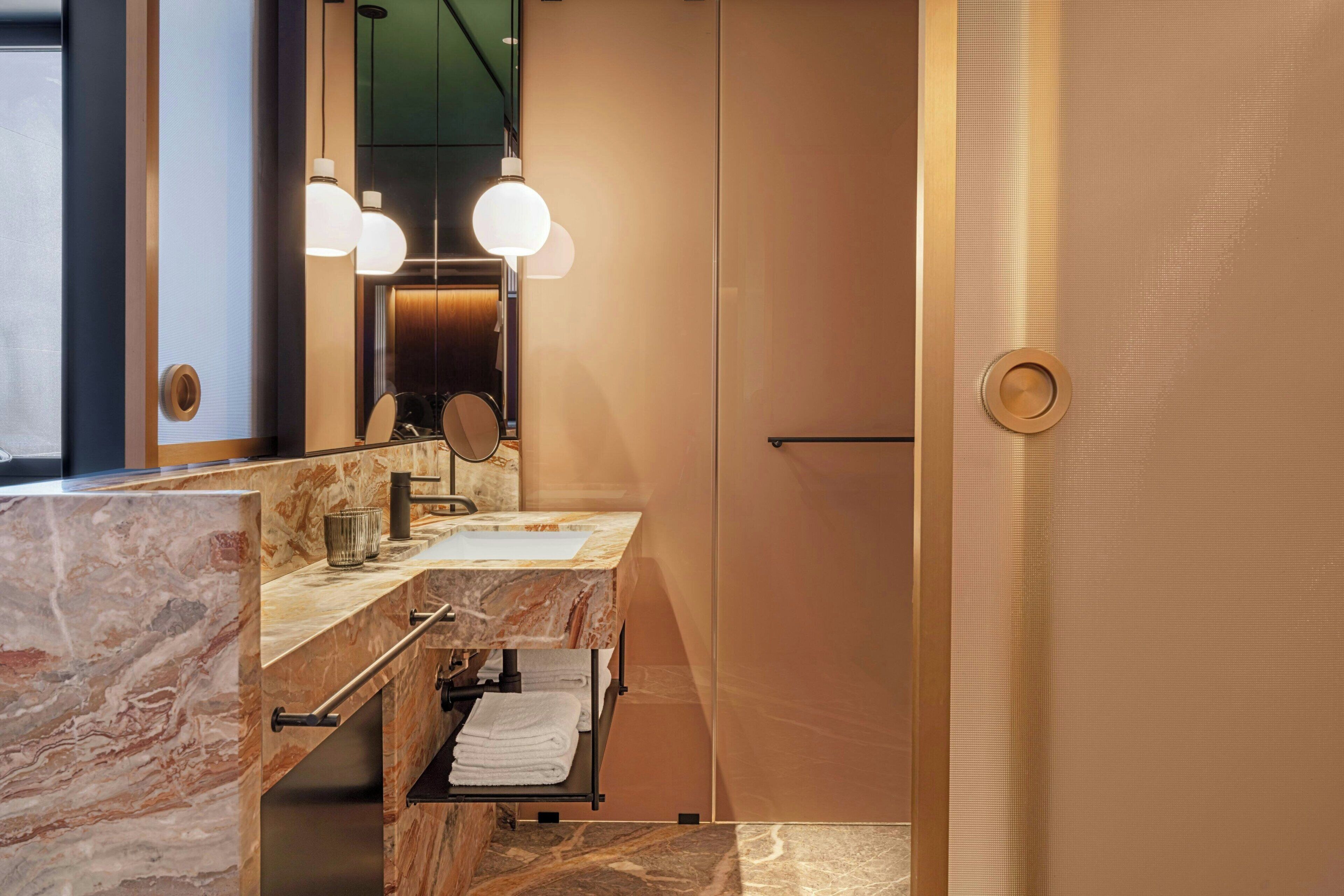 Un baño moderno con encimeras de mármol, un espejo grande y dos lámparas colgantes.