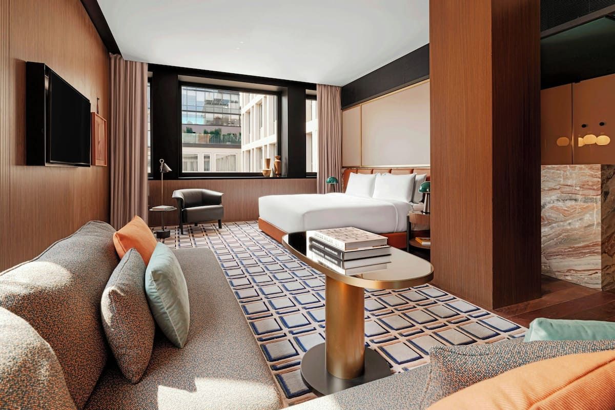 A hotel room with a sofa, a bed, a desk, a TV, and a window with a city view.