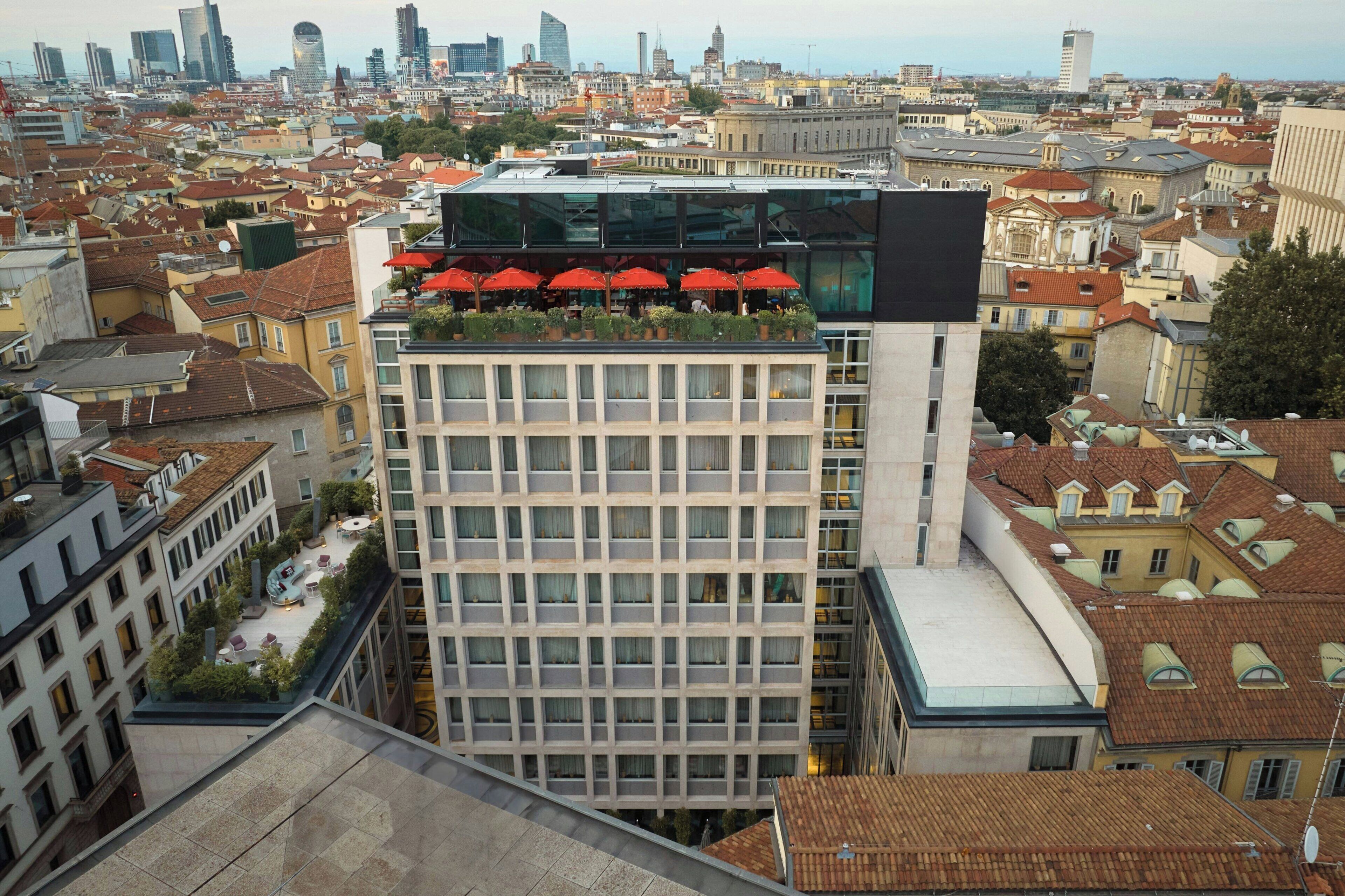 A high-rise building with a rooftop terrace featuring red umbrellas and potted plants.