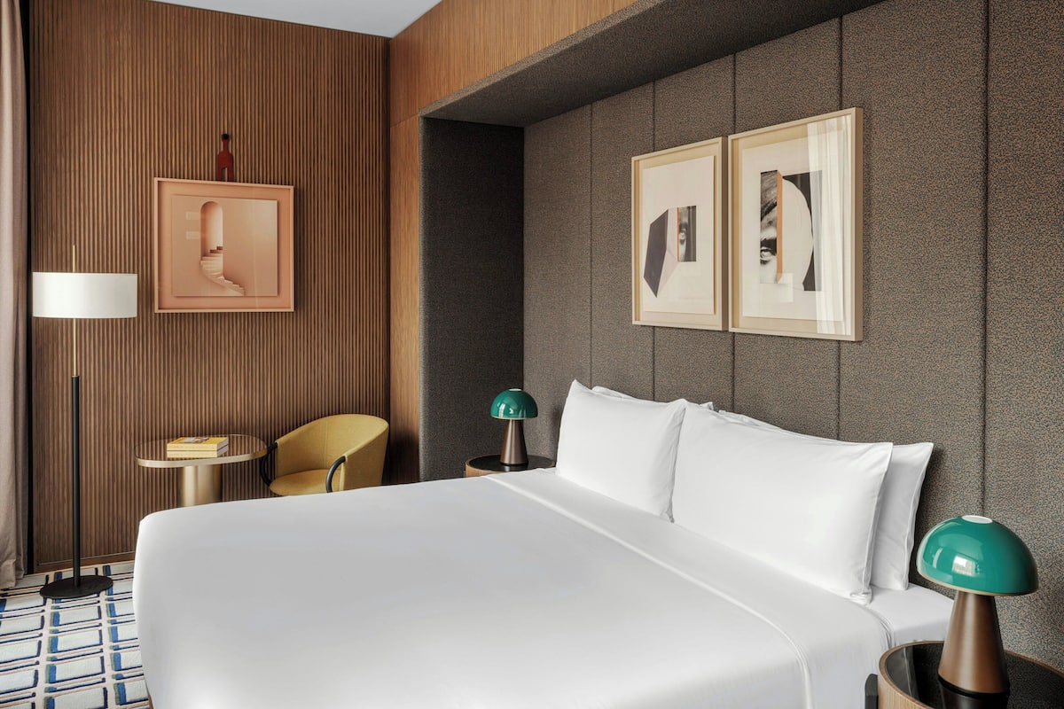 A hotel room with a large bed, two bedside tables, a chair, and artwork on the walls.
