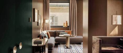 Una habitación de hotel moderna con un armario verde oscuro, un sofá, una mesita y una alfombra estampada.