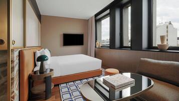 A hotel room with a bed, a TV, a window with a view, a table with books, and a chair.