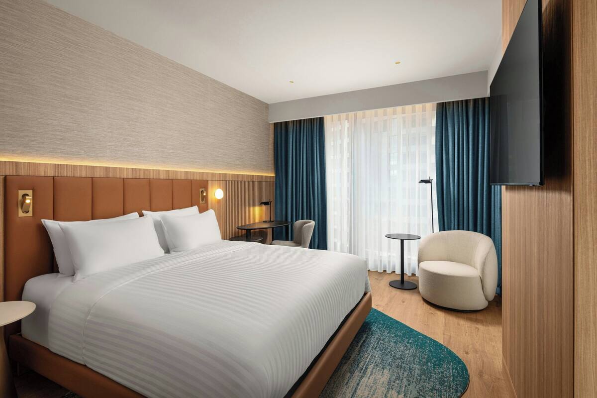Ein Hotelzimmer mit einem großen Bett, einem Schreibtisch, einem Sessel und einem an der Wand befestigten Fernseher.
