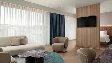 A modern hotel room with a sofa, armchair, and a TV mounted on the wall.