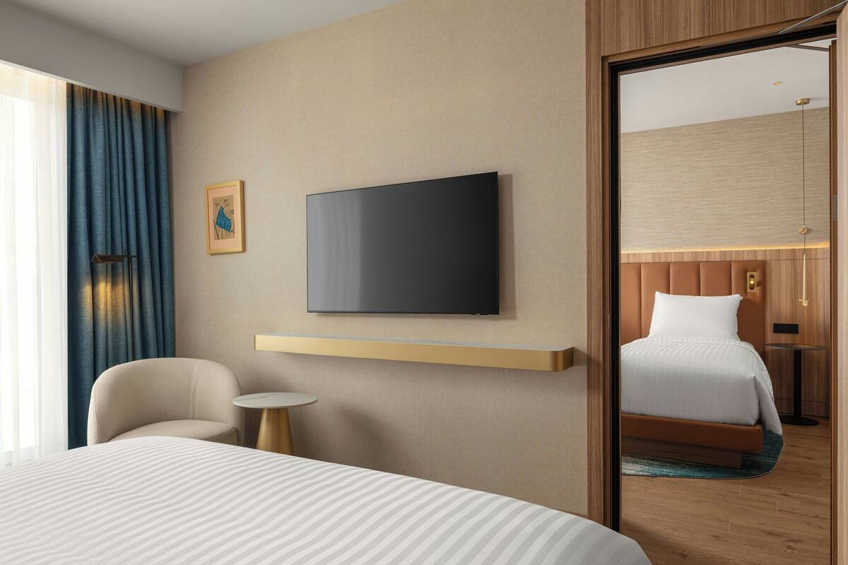 Ein Hotelzimmer mit Bett, einem an der Wand befestigten Fernseher, einem kleinen runden Tisch und einem Stuhl.