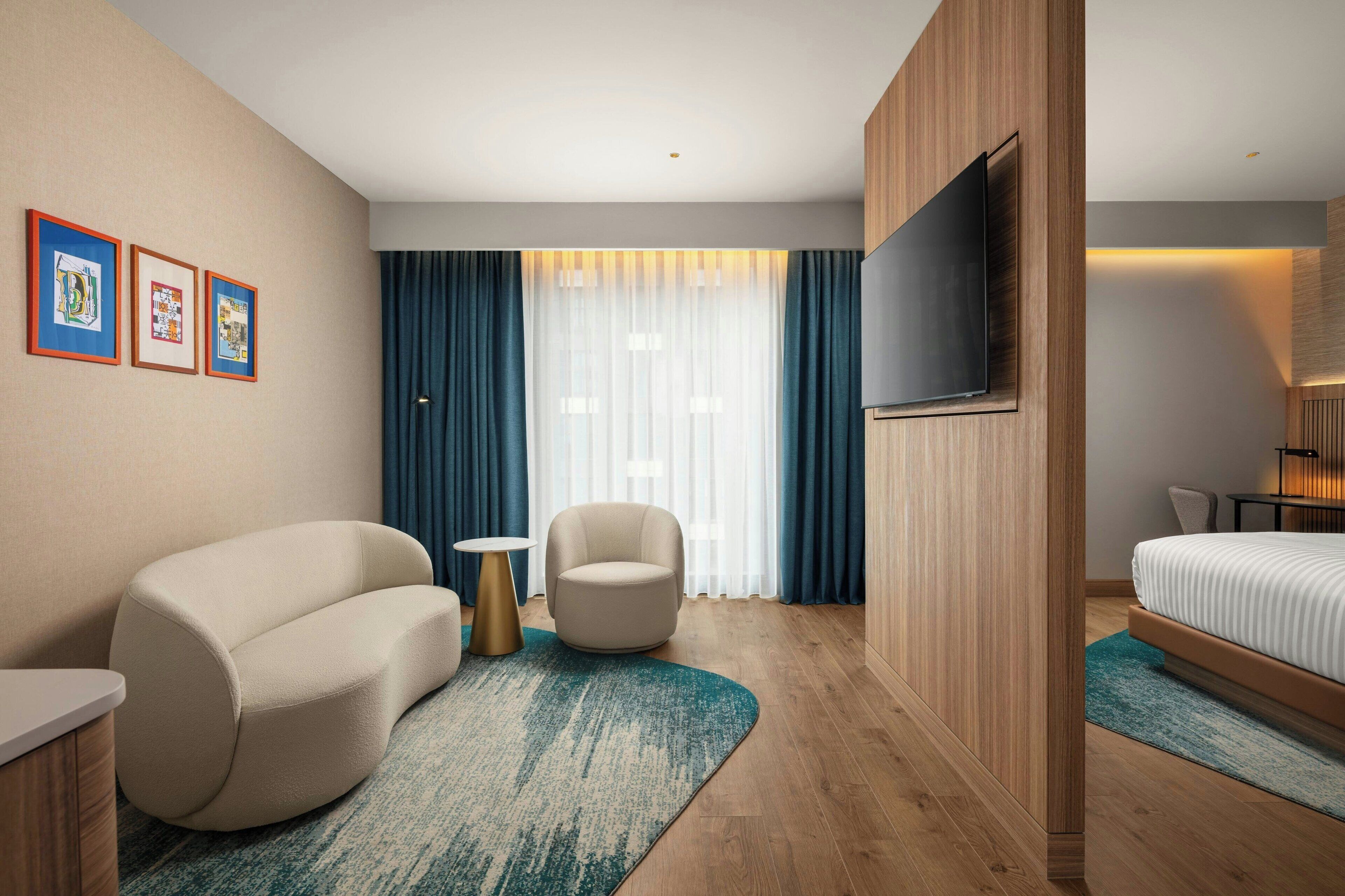 Ein modernes Hotelzimmer mit einer Couch, einem Sessel, einem kleinen runden Tisch und einem Bett.