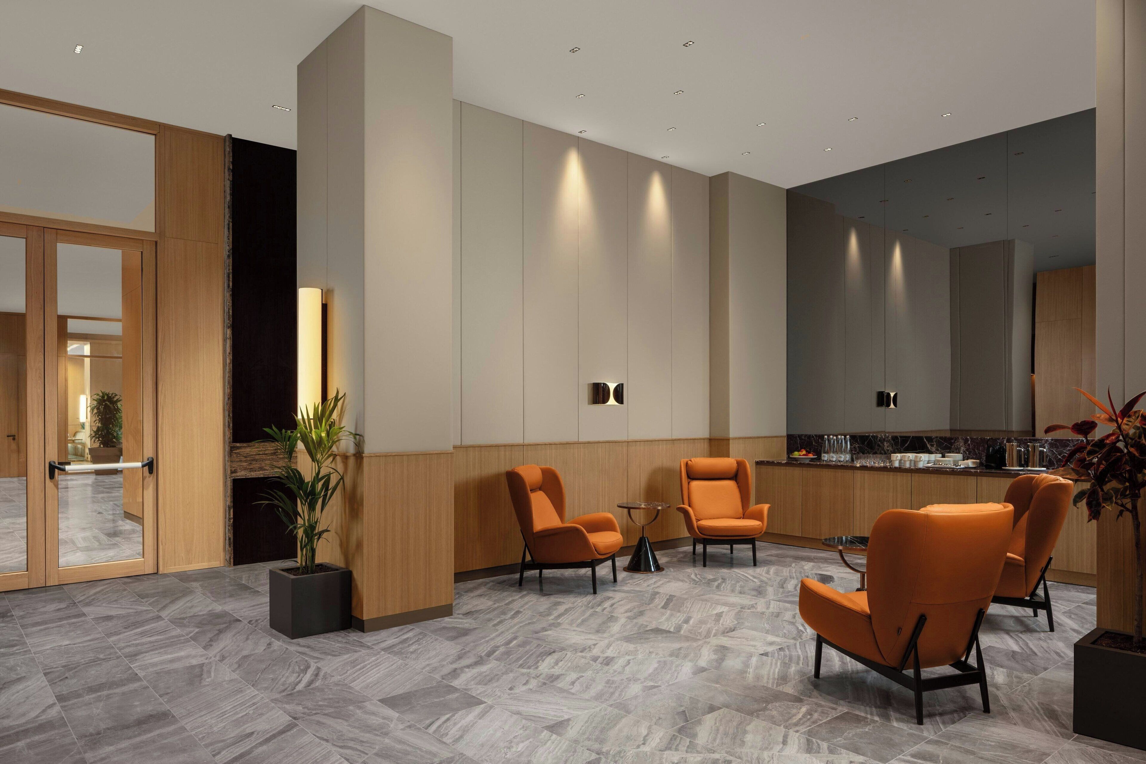 A modern hotel lobby with a seating area, a reception desk, and a kitchen in the background.
