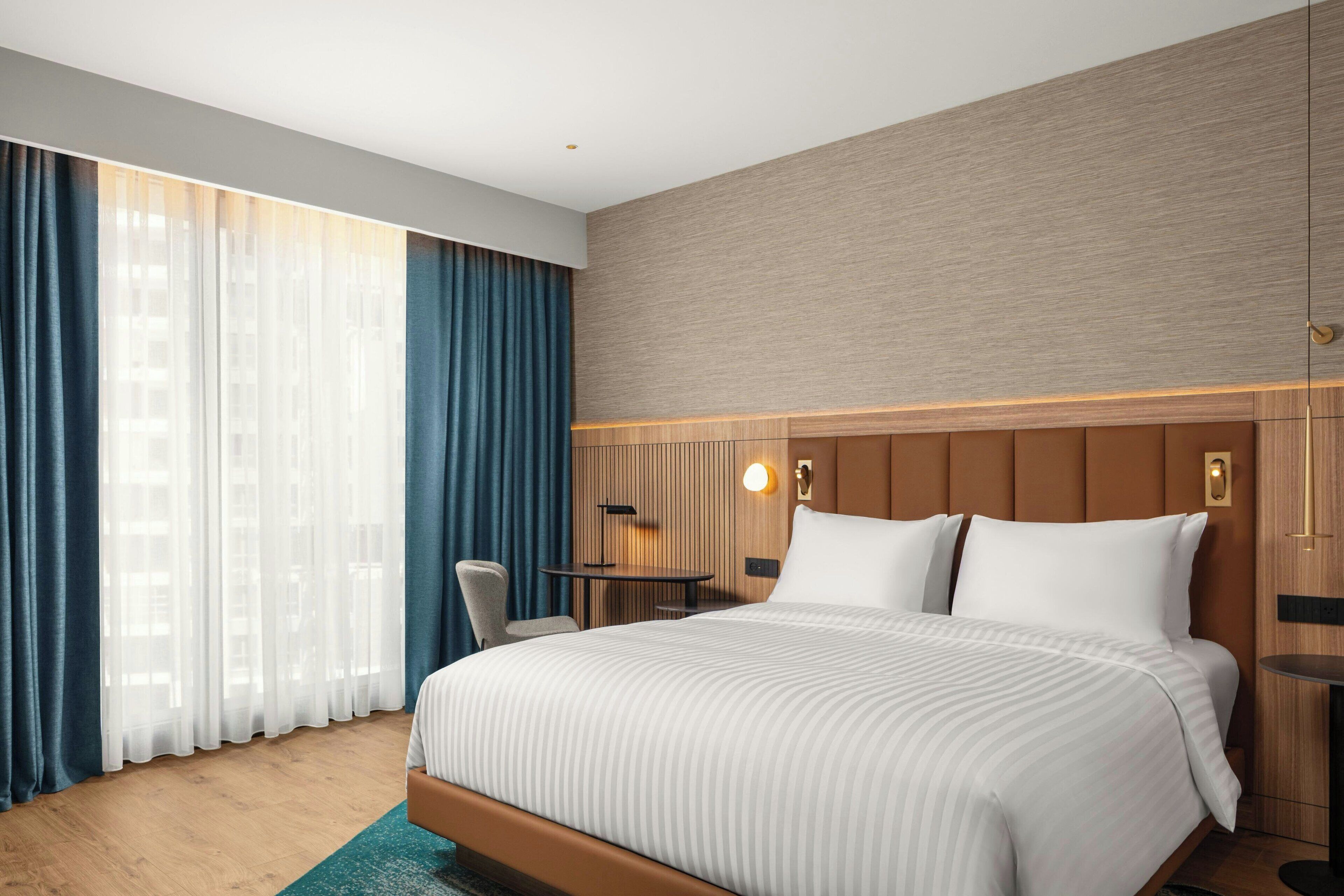 A modern hotel room with a large bed, a desk, and a chair.