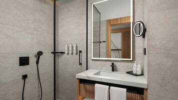 Un baño moderno con un espejo grande, ducha y tocador con artículos de aseo.