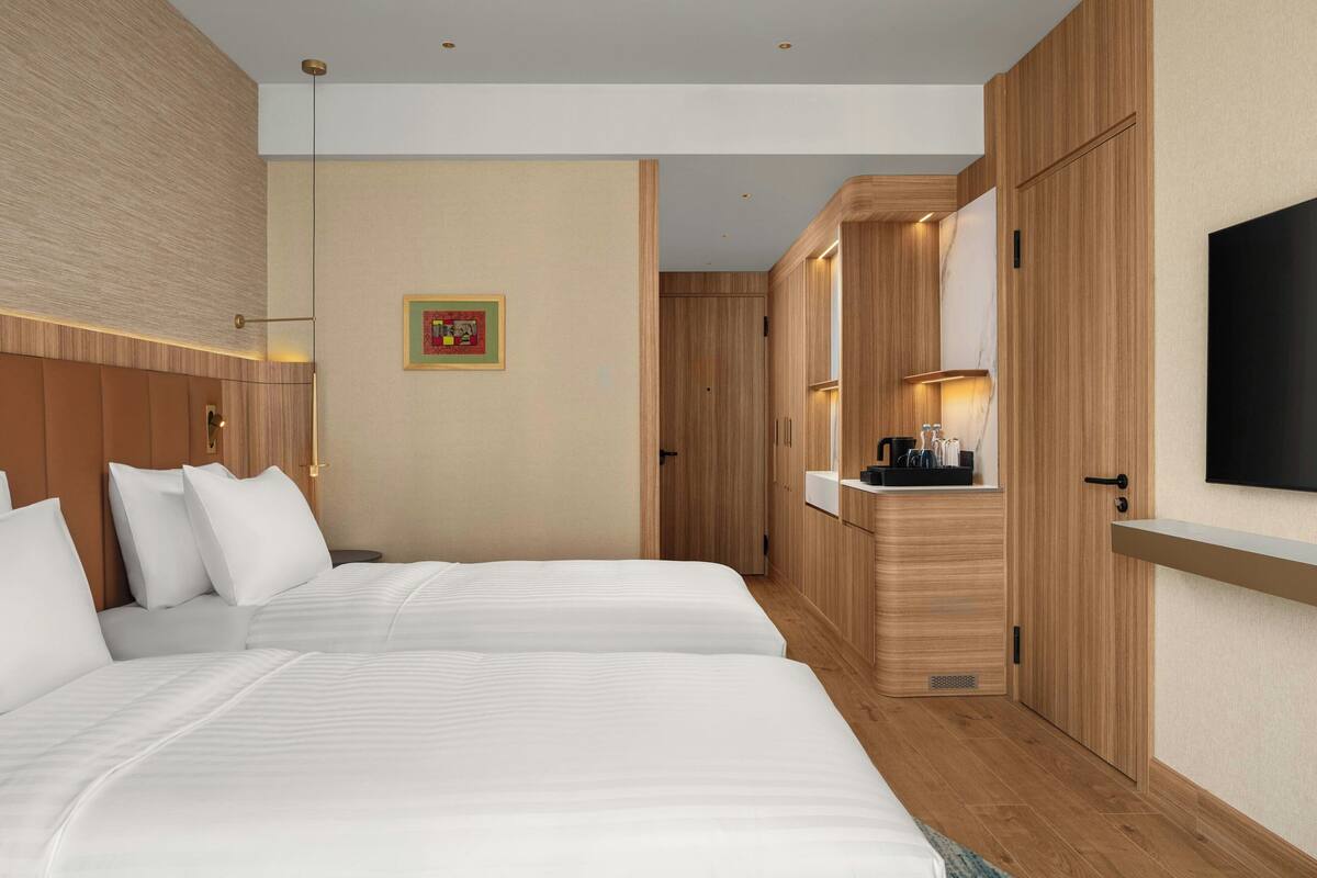 Ein Hotelzimmer mit zwei Betten, Holzvertäfelung, einem Wand-Fernseher und einer kleinen Küchenzeile.