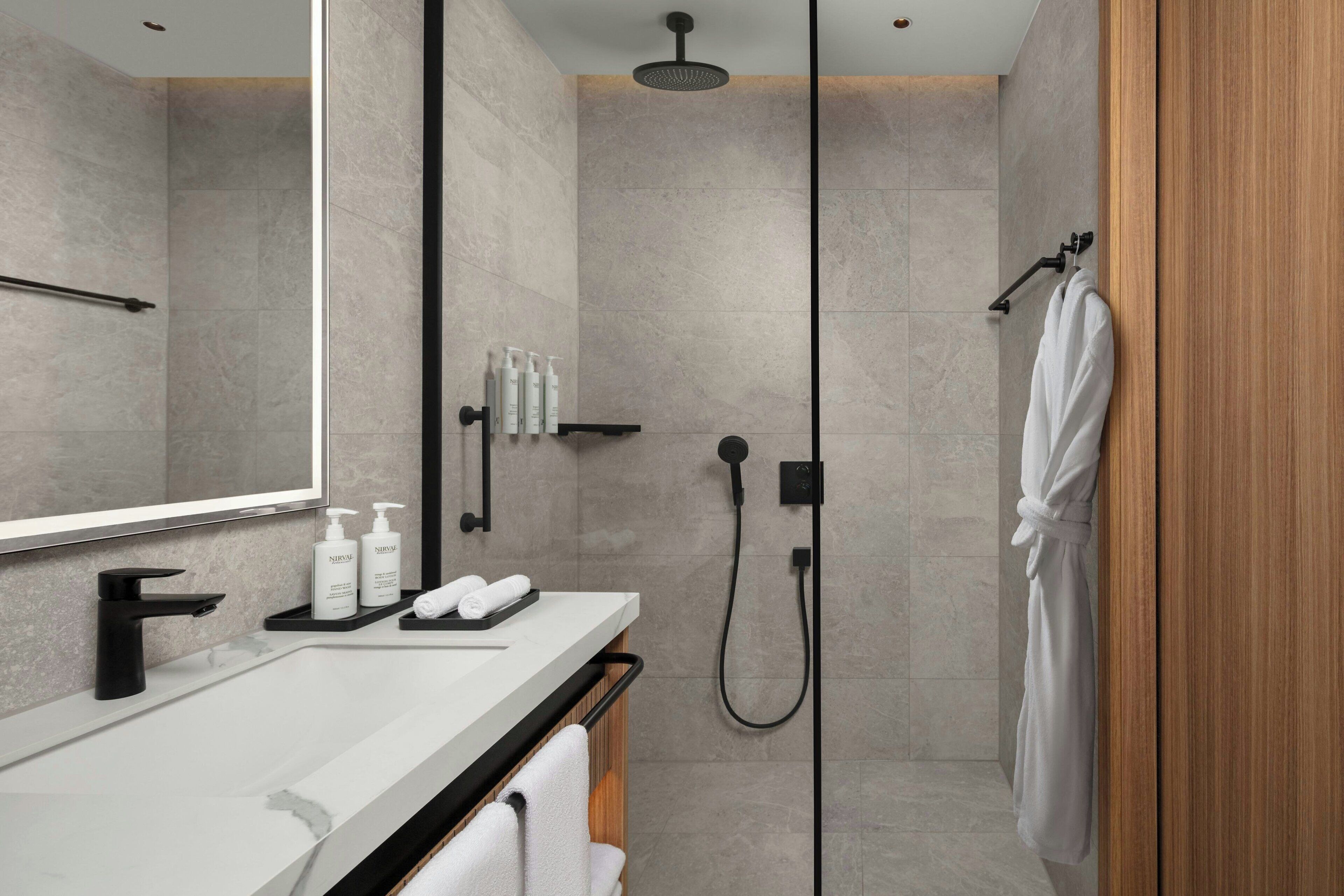 A modern bathroom with a large mirror, a black faucet, a shower with a handheld showerhead, and a wooden door.