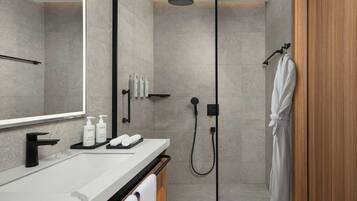 A modern bathroom with a large mirror, a black faucet, a shower with a handheld showerhead, and a wooden door.
