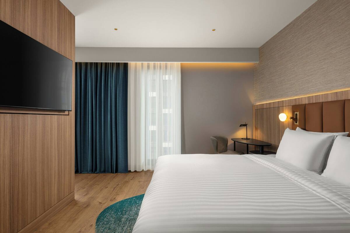 Ein modernes Hotelzimmer mit einem großen Bett, einem Flachbildfernseher, einem Schreibtisch und einer Lampe.