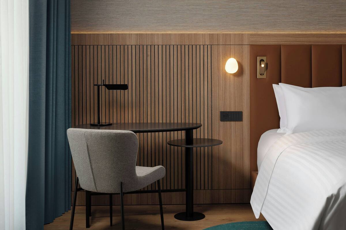 Ein Hotelzimmer mit einem Bett, einem runden Tisch, einem Stuhl, einer Lampe und einer Wandleuchte.