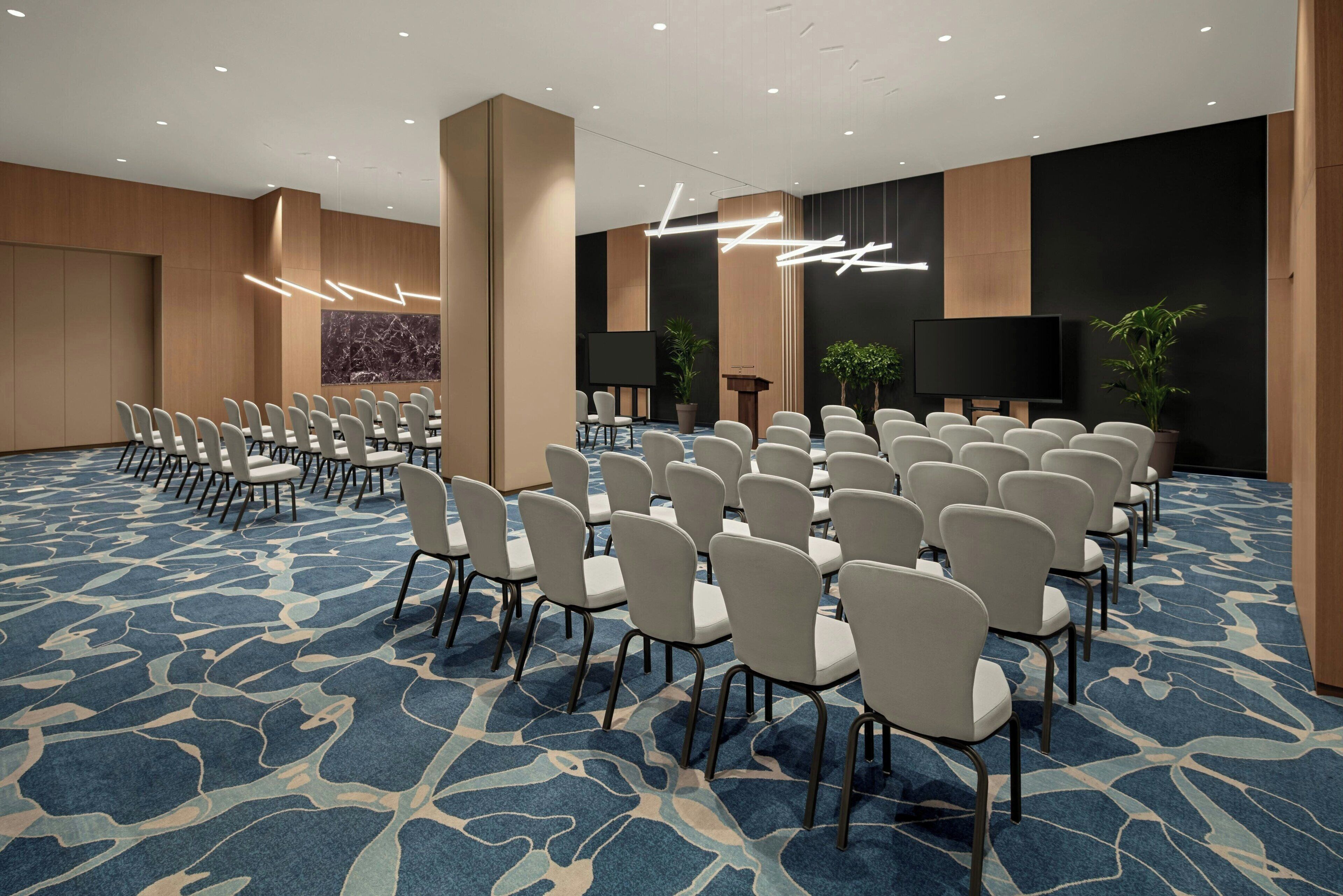 A conference room with rows of white chairs, a large screen, and a marble wall.