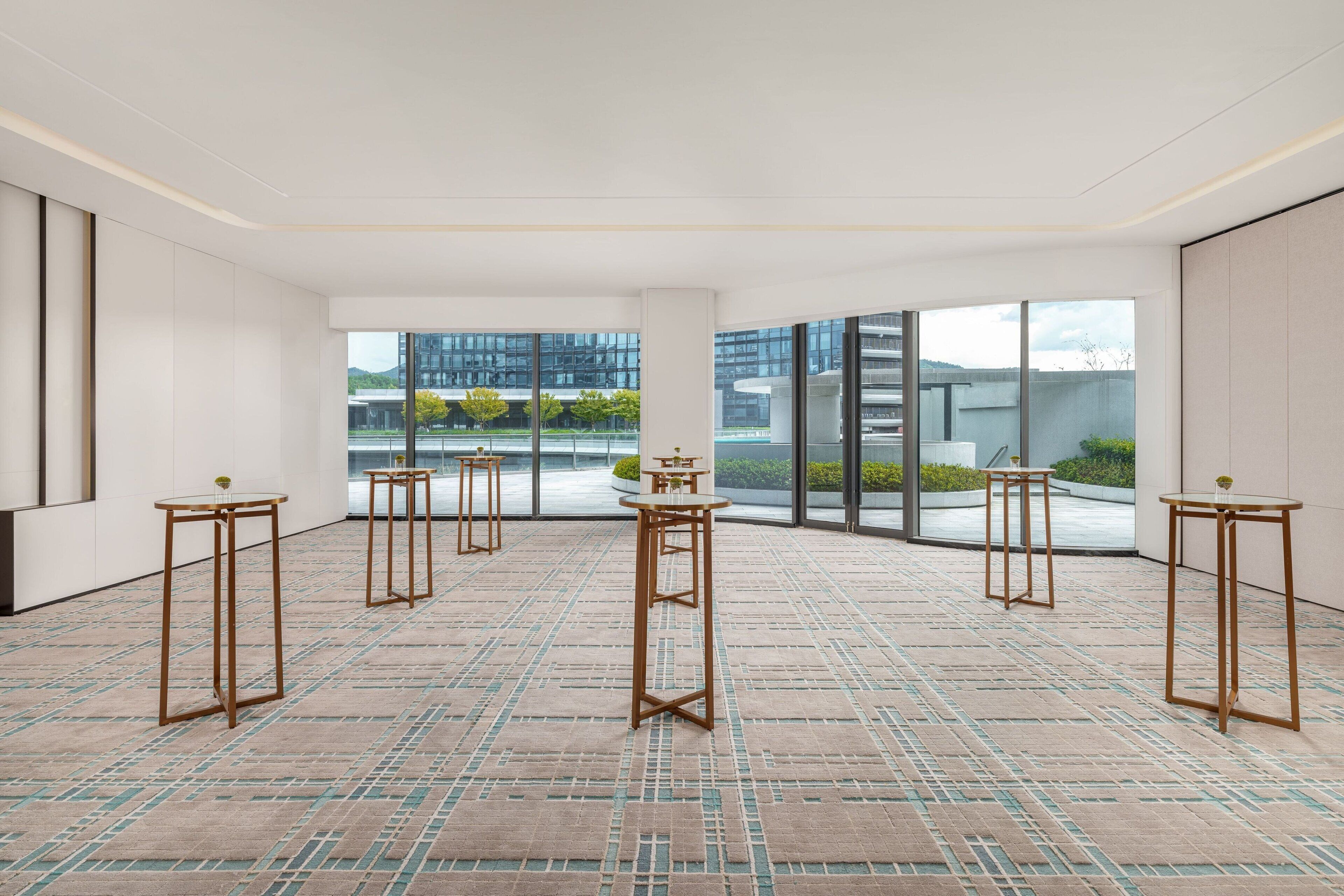 A spacious room with large windows, a patterned carpet, and several tall, slender tables.