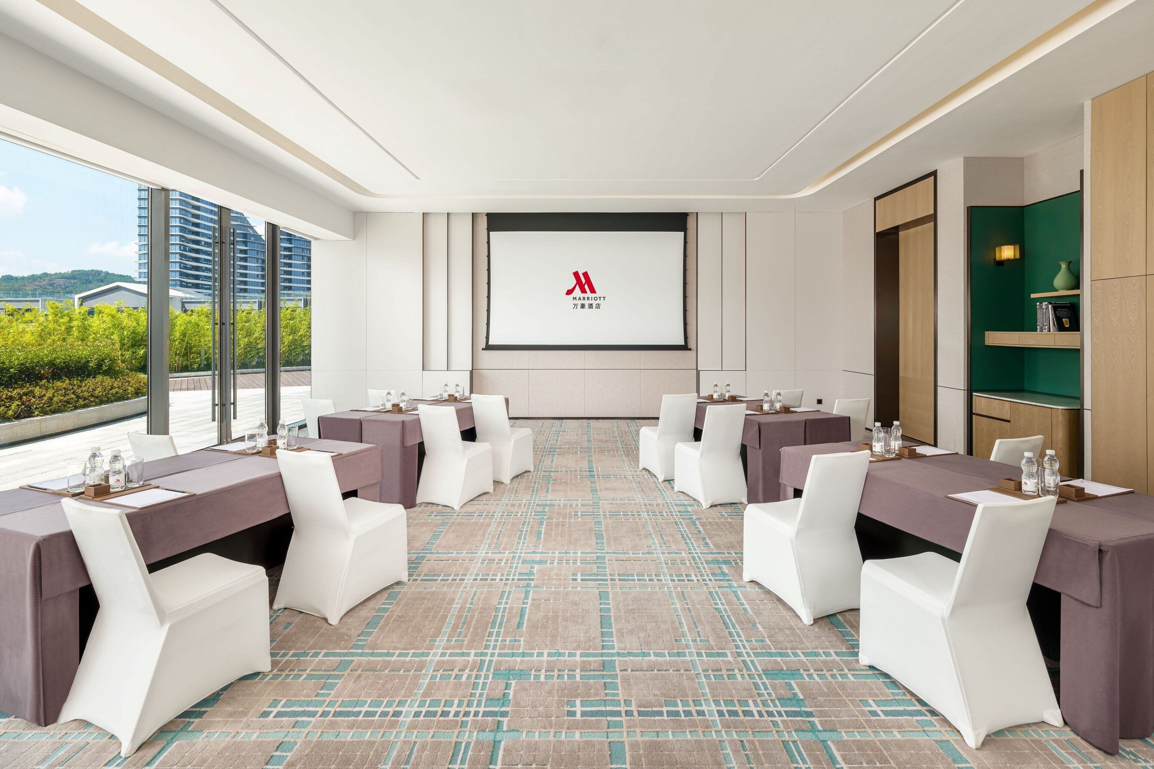 A conference room with a large screen displaying the Marriott logo, white chairs, and tables arranged for meetings.
