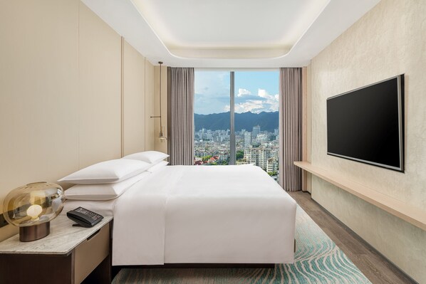 A hotel room with a large bed, a TV mounted on the wall, a nightstand with a lamp, and a view of a cityscape through a large window. - Lishui Marriott Hotel (Lishui)