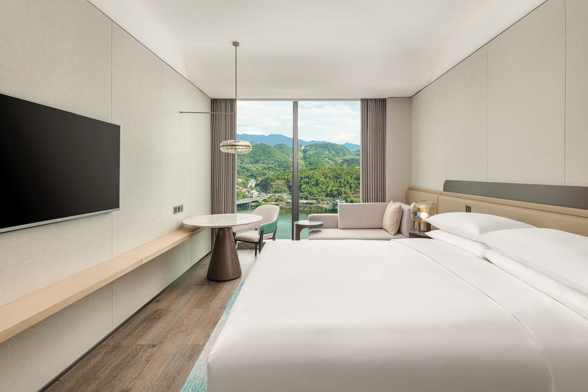 A modern hotel room with a large bed, a flat-screen TV, a small table, and a sofa.
