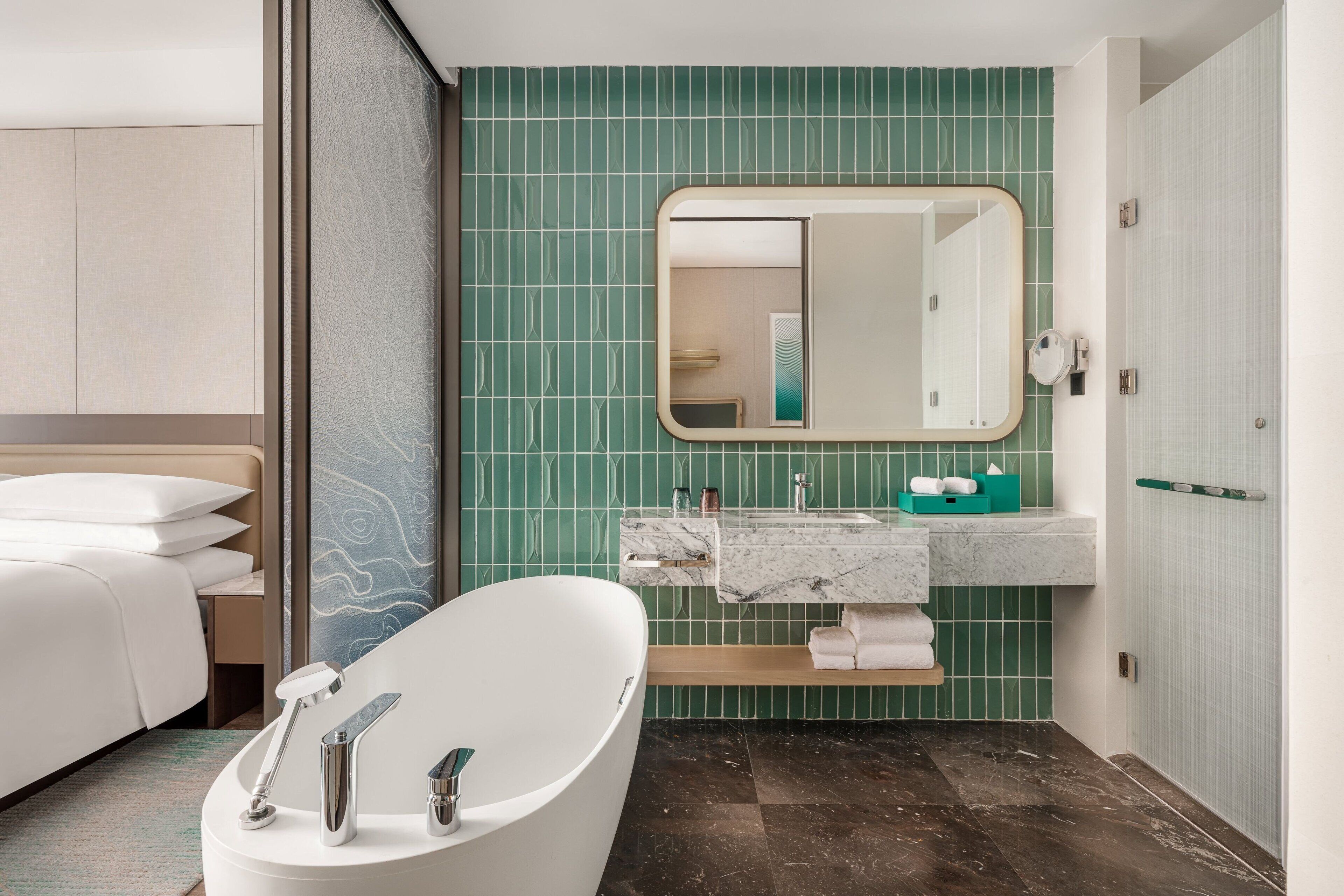 Un baño moderno con una bañera independiente, un tocador con espejo y paredes con azulejos verdes.