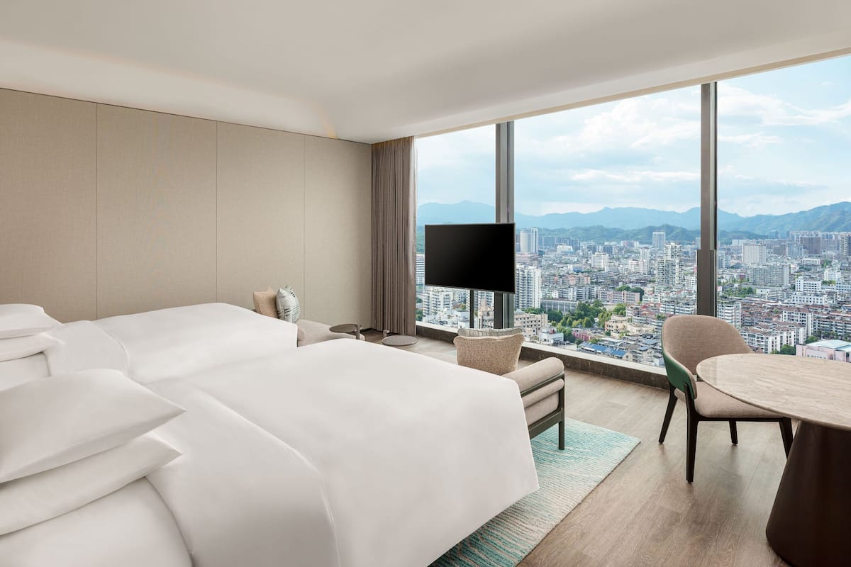 A hotel room with a large bed, a TV, a dining table, and a view of a cityscape.
