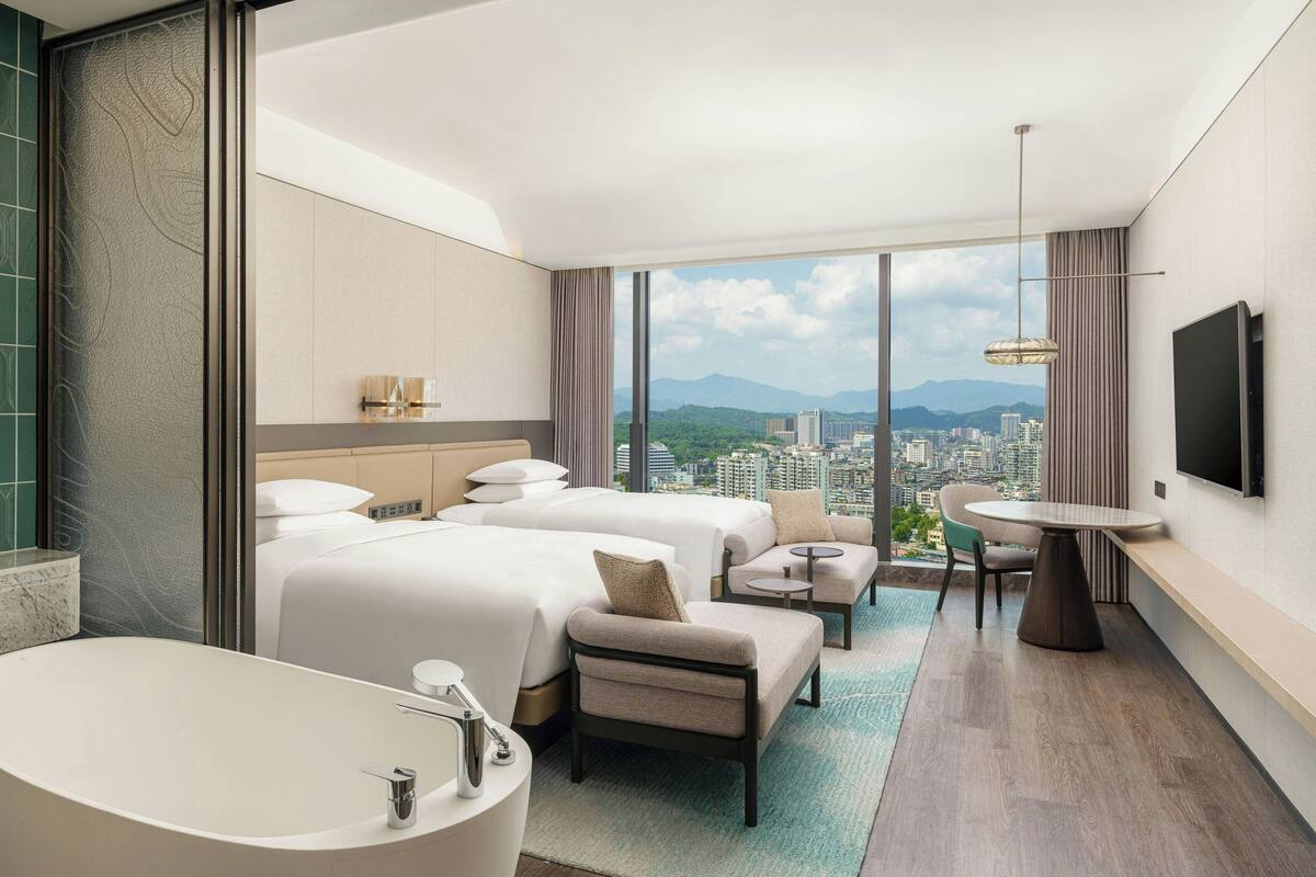 A hotel room with two beds, a large bathtub, a dining table, and a TV.