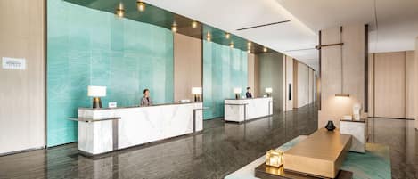 A modern hotel reception area with marble counters, teal accent walls, and a central seating area.