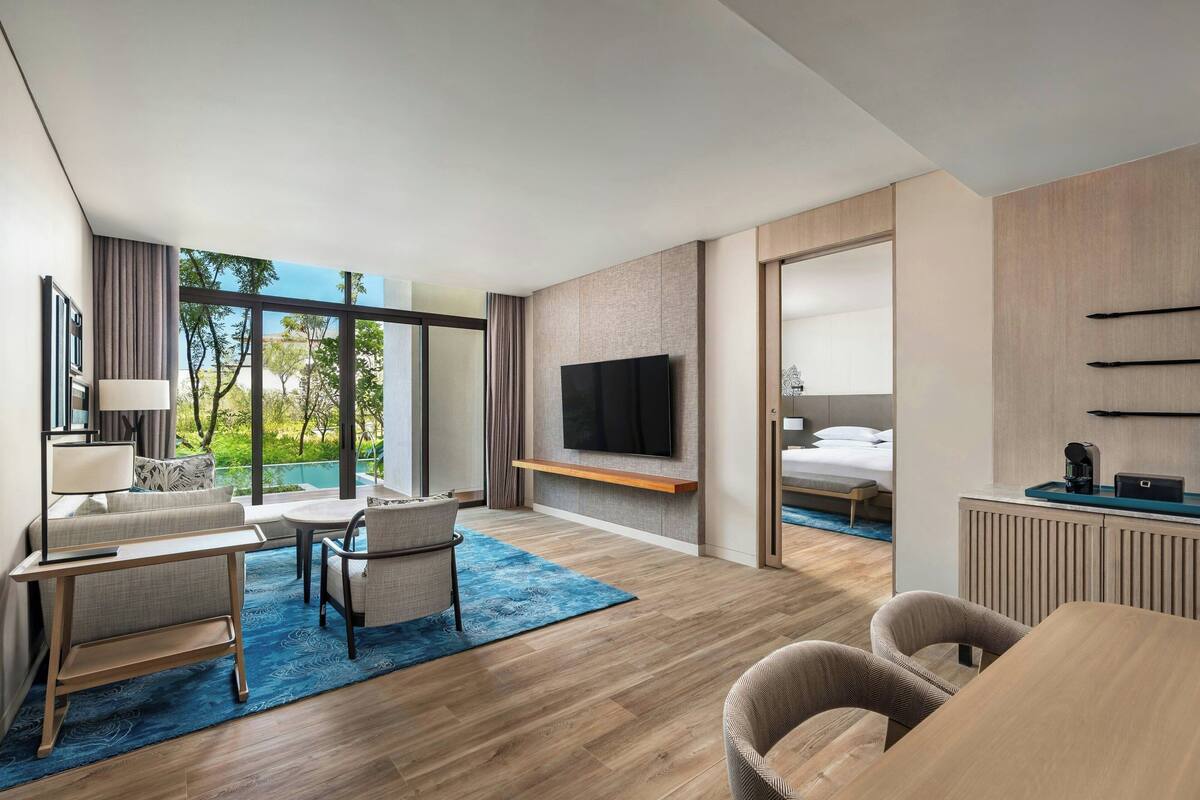 Una habitación de hotel moderna con un ventanal grande, un televisor de pantalla plana, un sofá, una mesa de comedor y una cama.