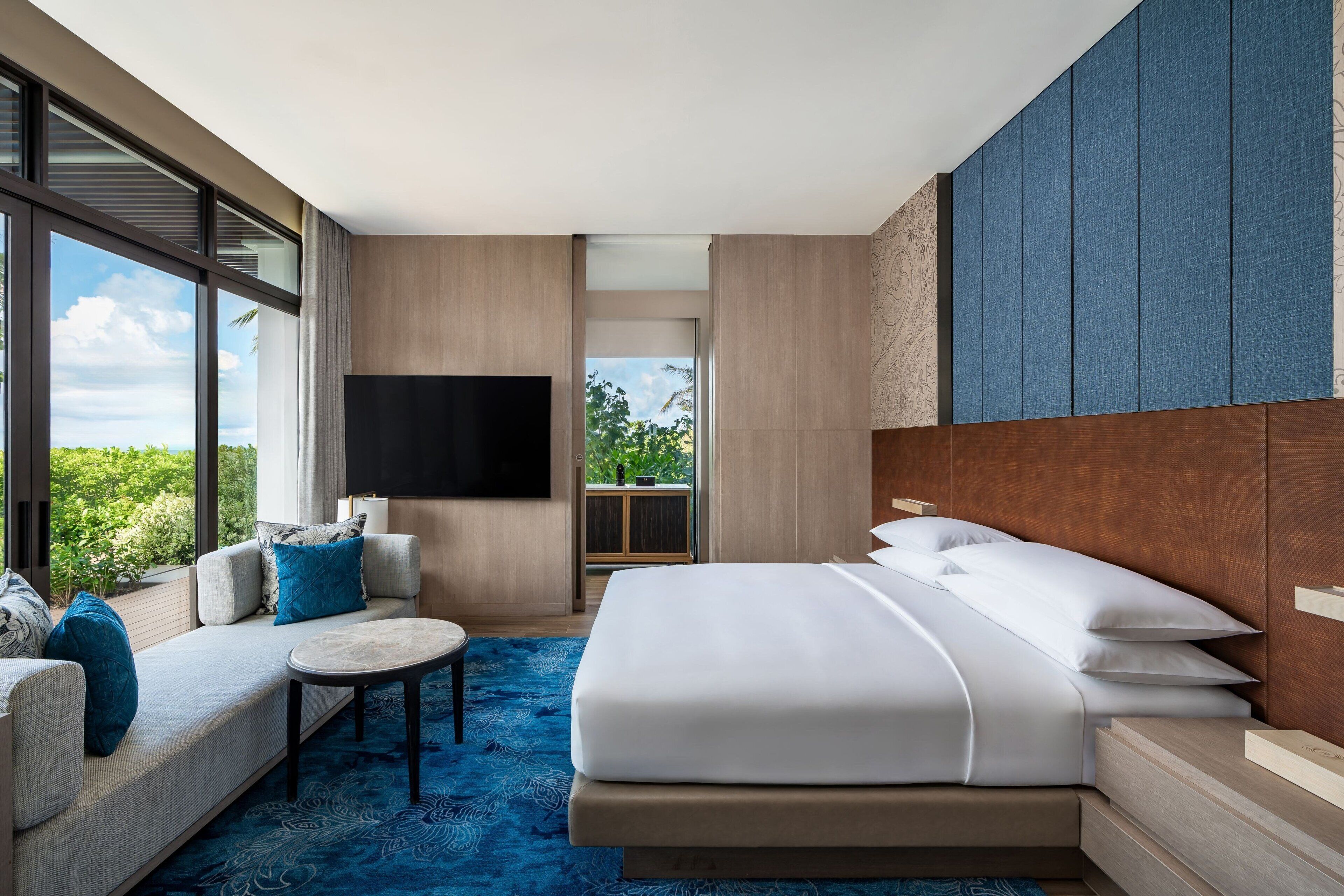 Una habitación de hotel moderna con una cama grande, un sofá, una mesita y un televisor.