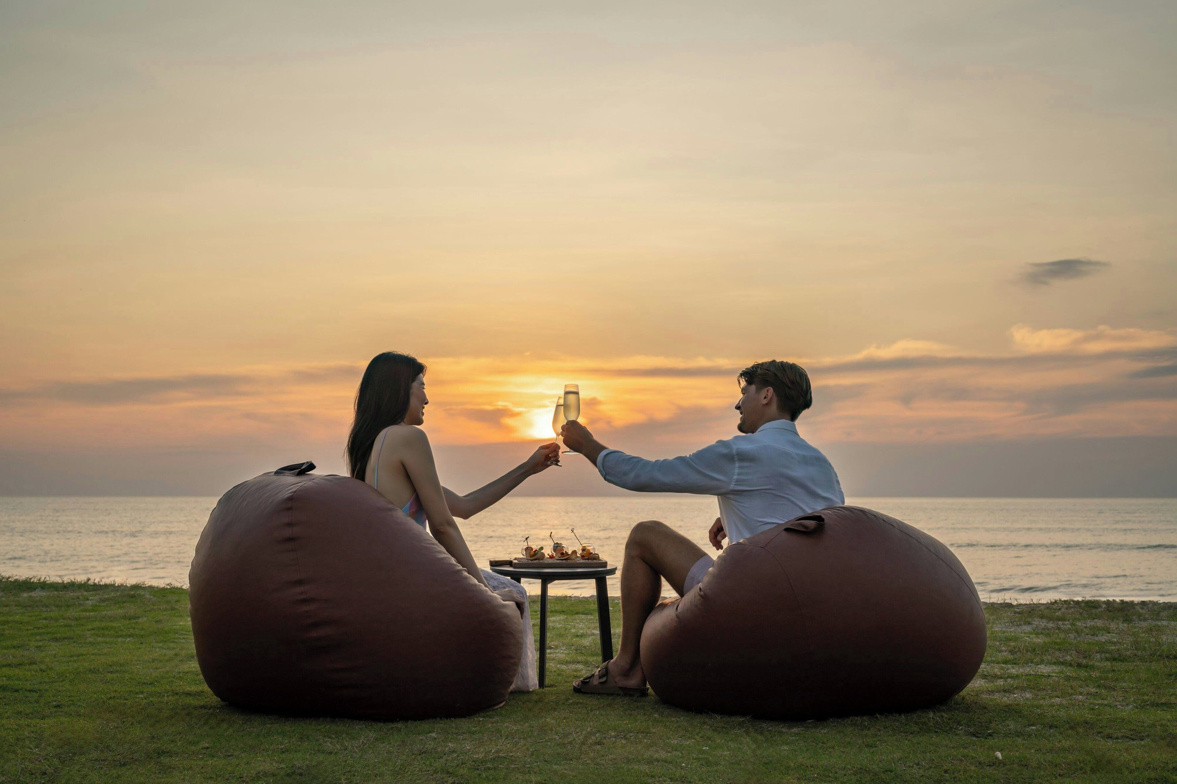 Two people sitting on bean bags facing a sunset over the ocean.
