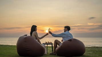 Two people sitting on bean bags facing a sunset over the ocean.