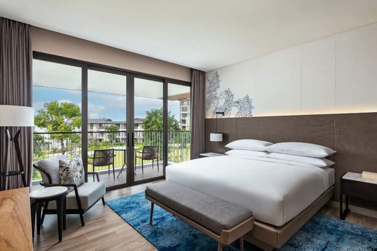 Una habitación de hotel moderna con una cama grande, un banco, un escritorio y un balcón con vistas a la ciudad.