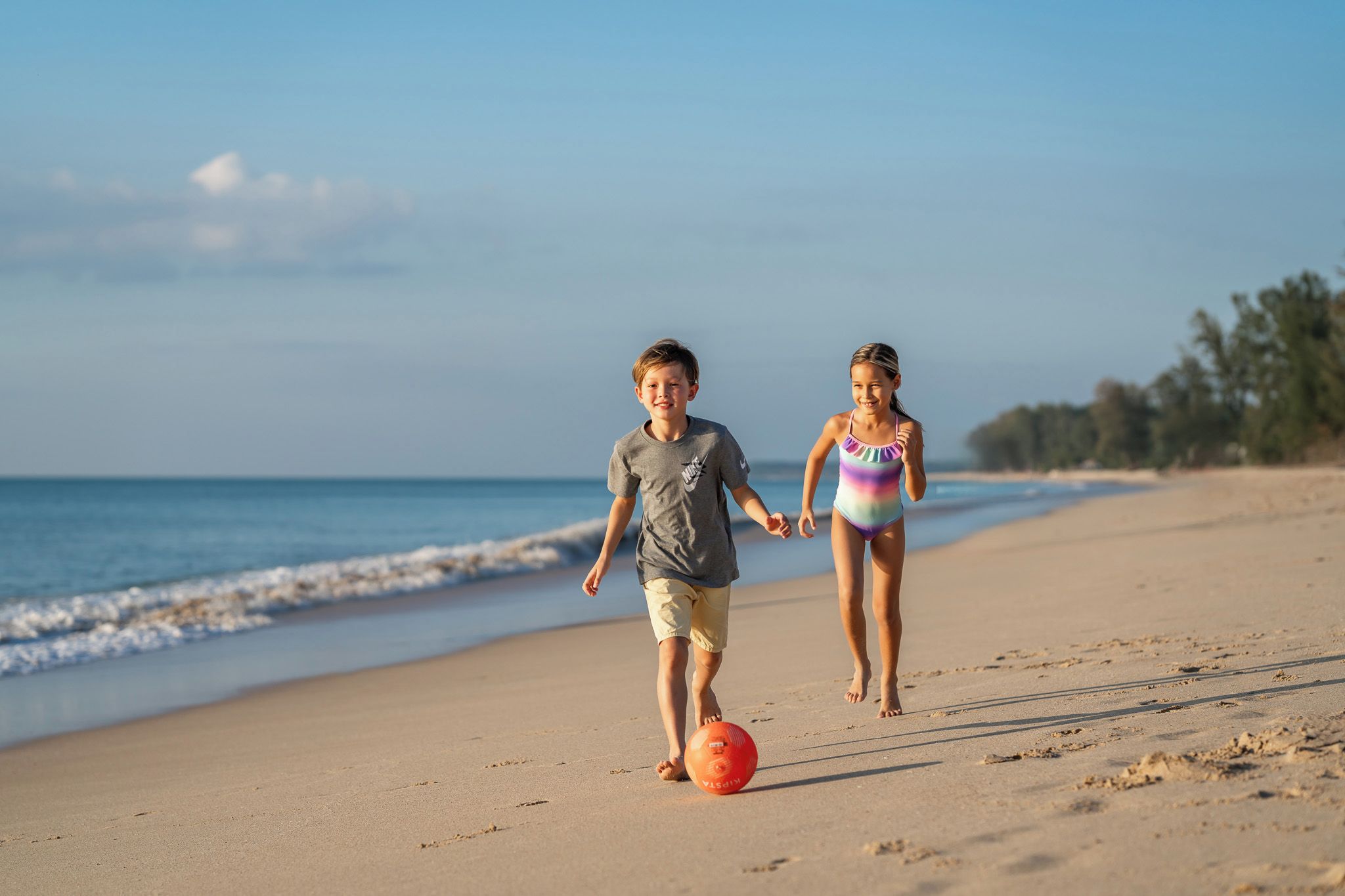 Two children playing with a ball on a sandy beach with the ocean in the background.