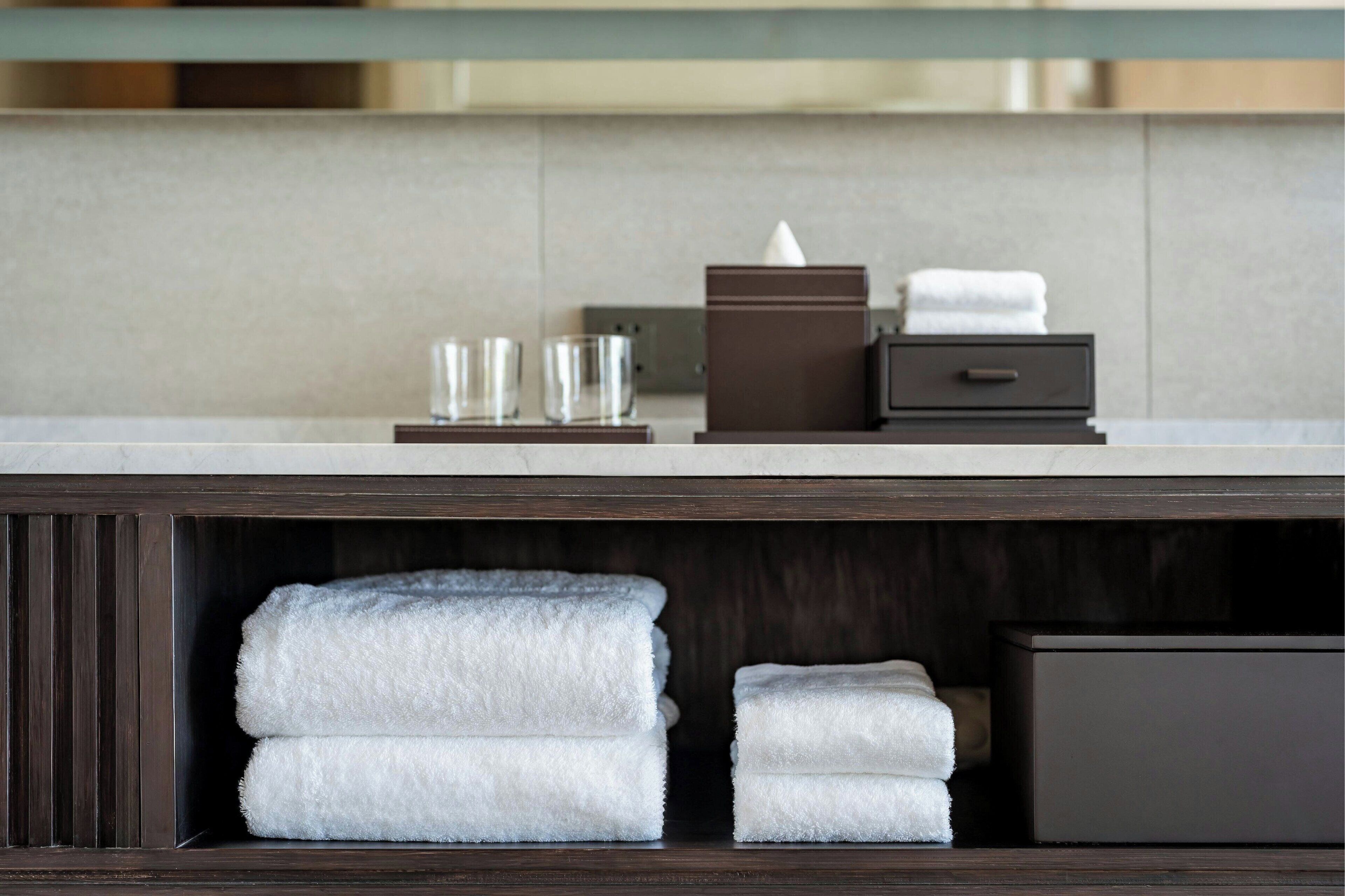 Een hotelbadkamer met een donker houten wastafelmeubel, een spiegel en netjes opgevouwen handdoeken.
