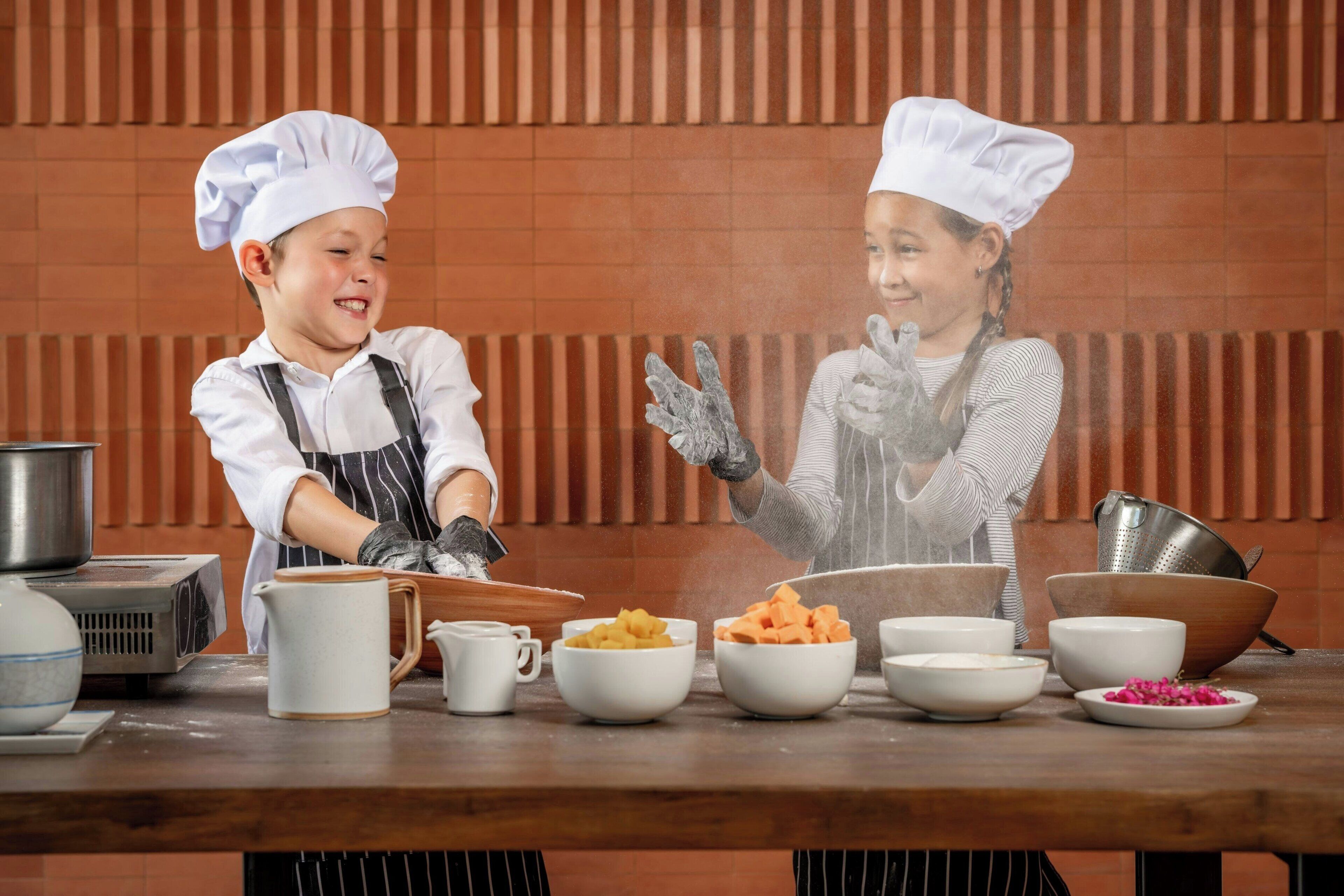 Twee personen in koksmutsen en schorten, die met eten aan een keukenblad werken.