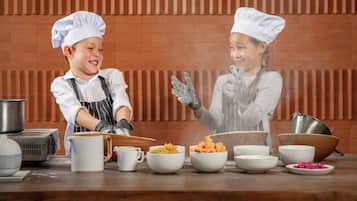 Twee personen in koksmutsen en schorten, die met eten aan een keukenblad werken.