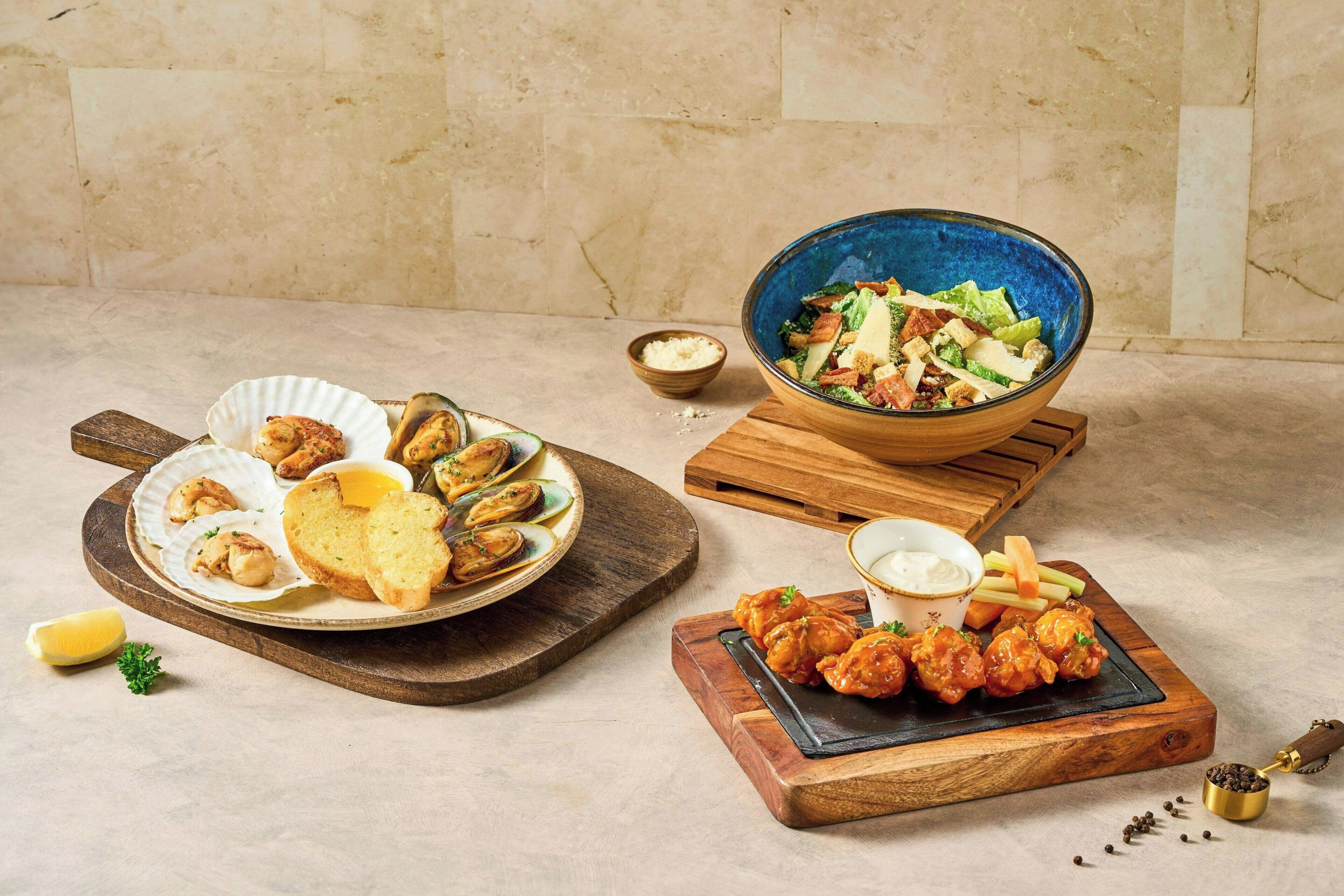 A variety of seafood dishes, including mussels, bread, and a salad, served on wooden boards.