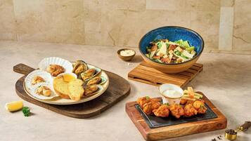 A variety of seafood dishes, including mussels, bread, and a salad, served on wooden boards.